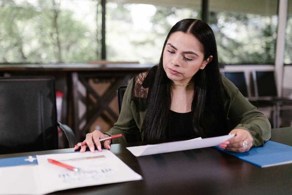 A professional reviewing documents and charts at a desk with a red pen