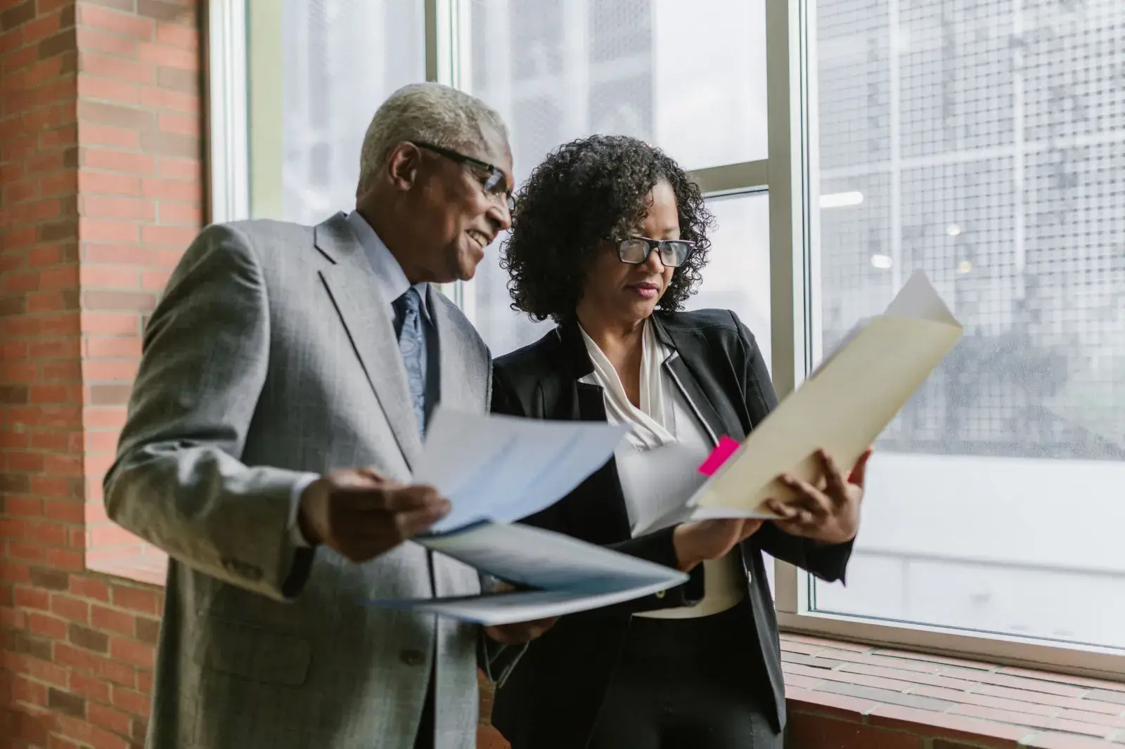 Two professionals standing by a window reviewing documents in folders